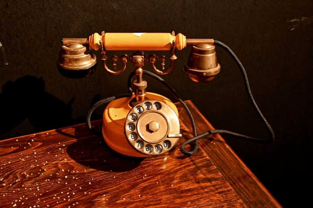 Antique rotary telephone with dual earpieces on a wooden desk, representing early telephone invention.