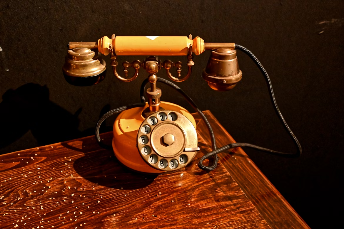 Antique rotary telephone with dual earpieces on a wooden desk, representing early telephone invention.