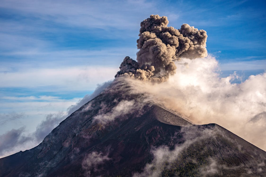 Stratovolcano erupting with a dense ash plume rising into the stratosphere against a blue sky.