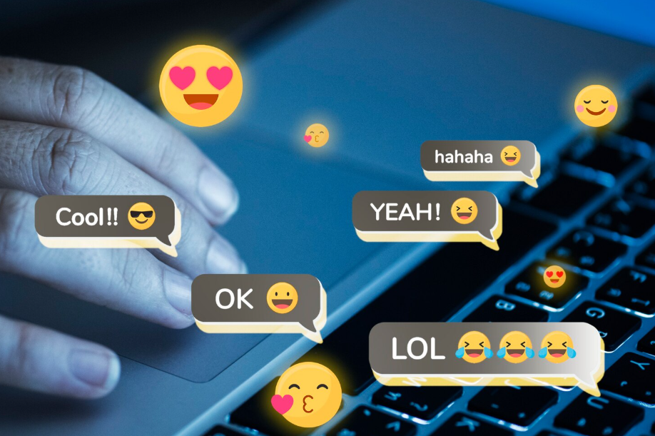 Hand typing on a laptop with floating chat bubbles and emojis, including heart eyes and sunglasses.