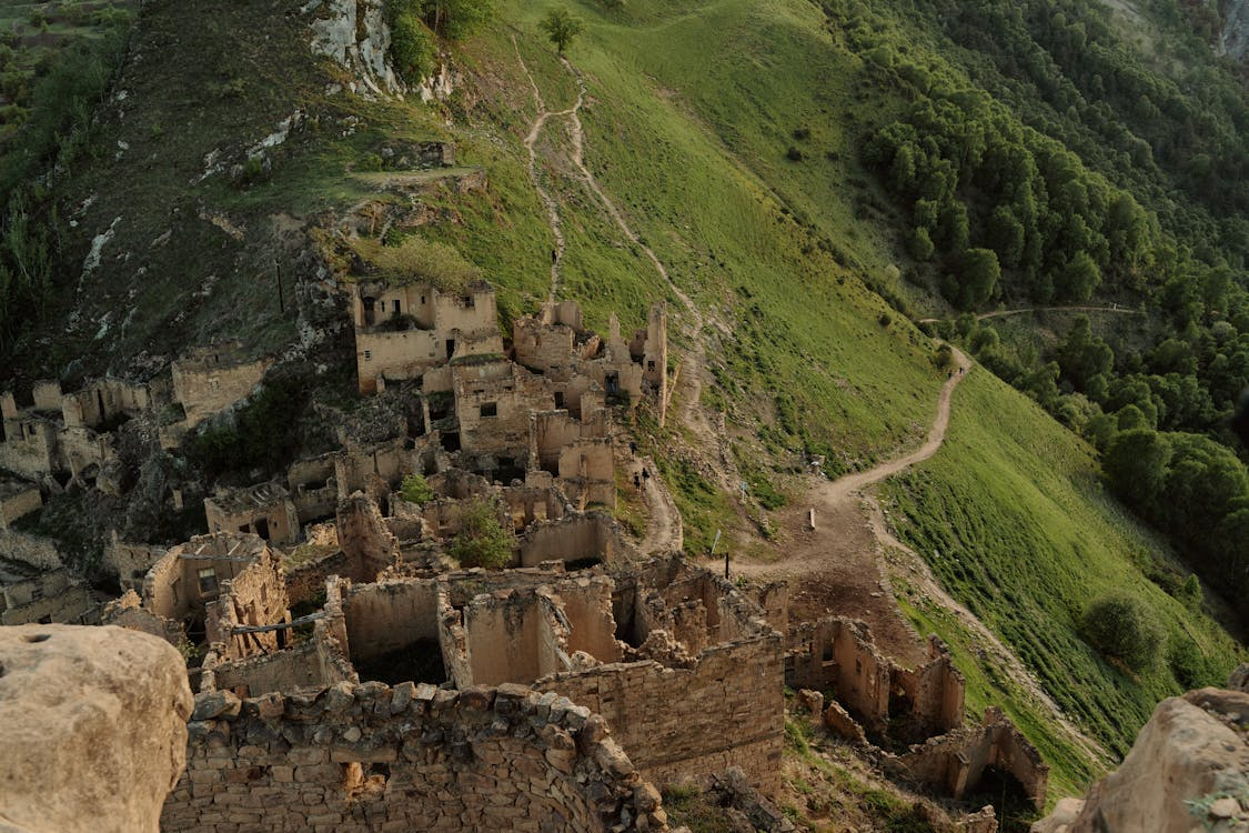 Aerial view of stone building ruins on a green hillside, showing a deserted mountain town.