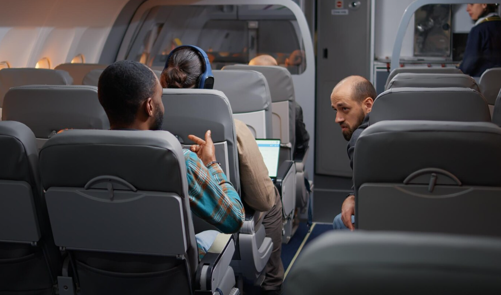 Airline cabin with travelers chatting across the aisle, illustrating airplane etiquette rules about noise.