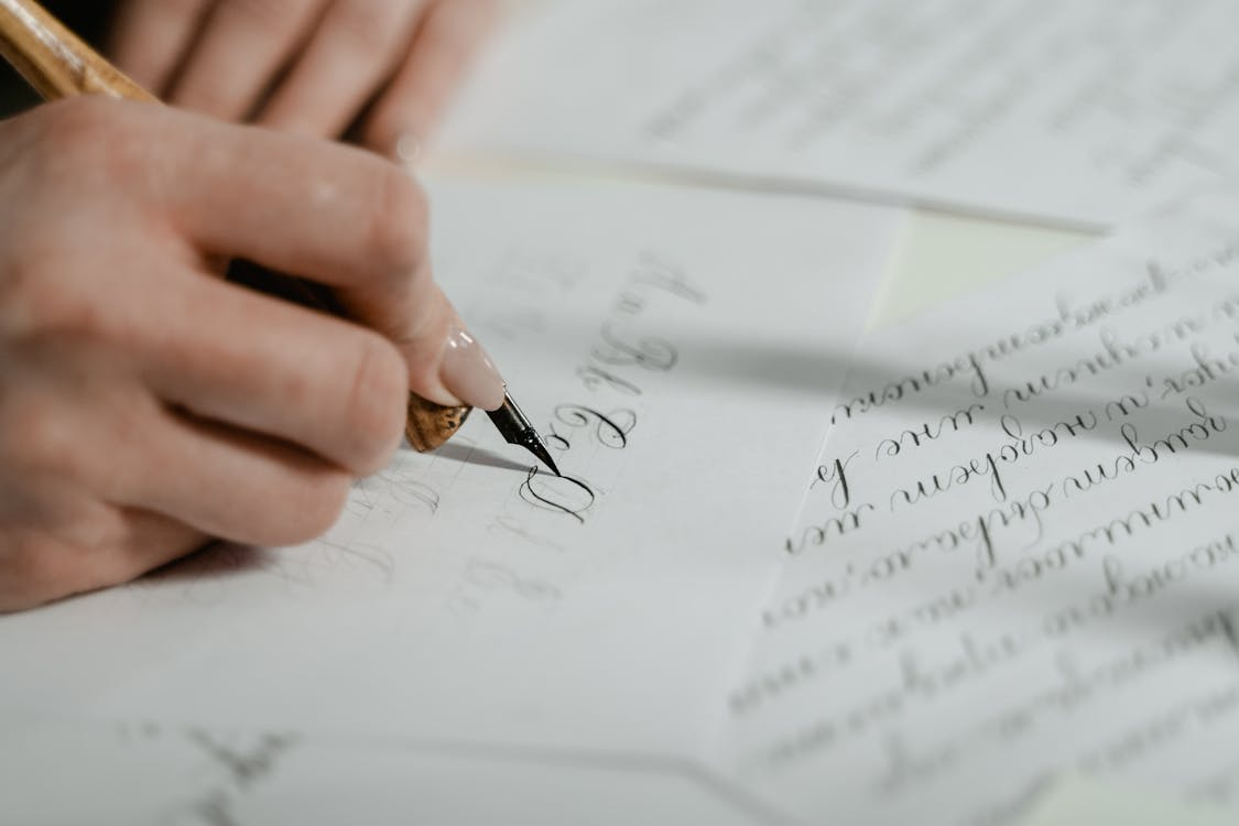 Close-up of a hand using a dip pen to write elegant cursive letters, illustrating handwriting psychology.