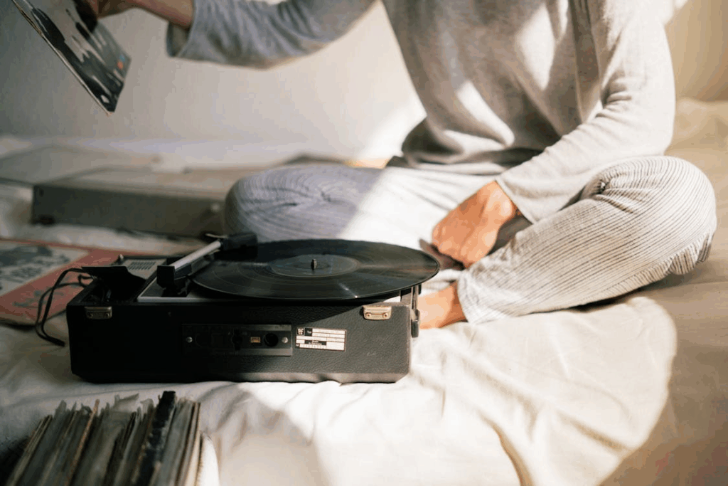 Analog nostalgia on a lazy morning with a person choosing a record beside a portable turntable and vinyl sleeves.