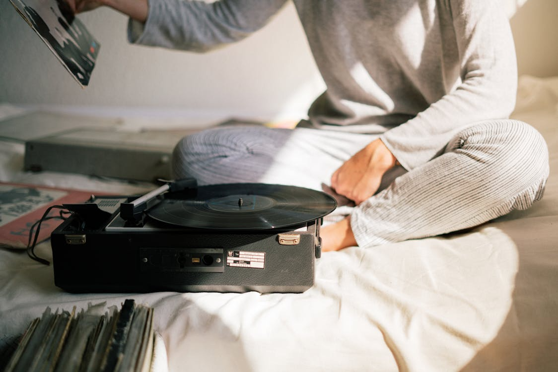 Analog nostalgia on a lazy morning with a person choosing a record beside a portable turntable and vinyl sleeves.