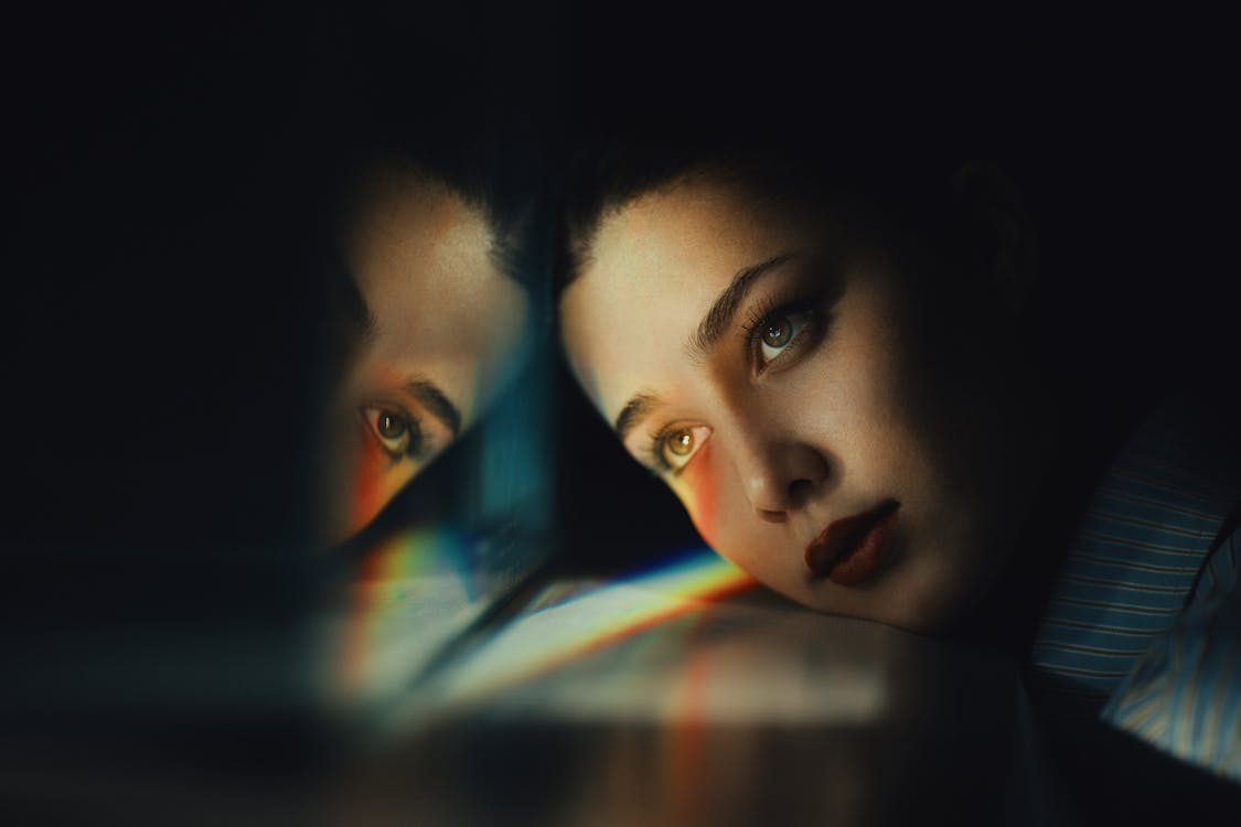 Woman gazing at her reflection with soft prism light, symbolizing inner monologue.