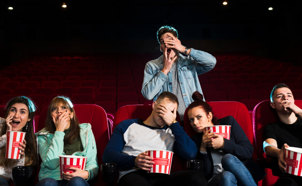 Audience flinching in a cinema during a tense scene of a disaster movie.