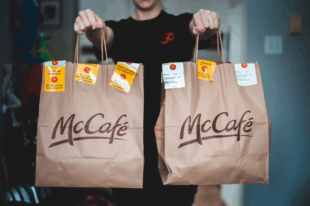 Person holding two McCafé takeout bags, illustrating fast food culture and to-go convenience.