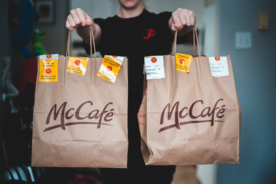 Person holding two McCafé takeout bags, illustrating fast food culture and to-go convenience.